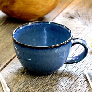 Puede incluir: Una taza de cer&aacute;mica azul con un borde oscuro y un asa. La taza est&aacute; sobre una superficie de madera.