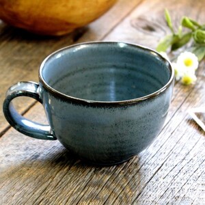 Puede incluir: Una taza de cer&aacute;mica azul con un borde marr&oacute;n oscuro. La taza est&aacute; sobre una superficie de madera.