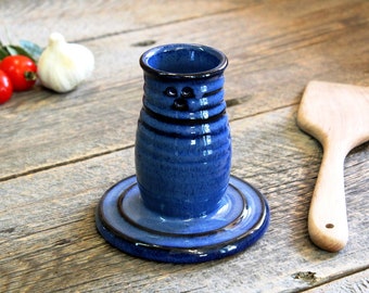 May include: A blue ceramic salt cellar with a small base and a round opening at the top. The cellar has a black rim and three small holes on the side.