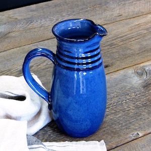 May include: A blue ceramic jug with a wide mouth and a handle. The jug has a glossy finish and a dark blue rim.