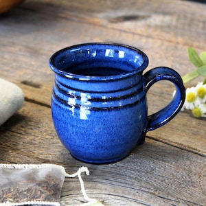 May include: A blue ceramic mug with a rounded body and a handle. The mug has a speckled glaze and a dark blue rim.
