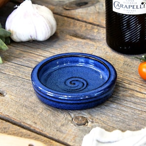 May include: A small, blue ceramic dish with a swirl design. The dish is perfect for serving small snacks or condiments.