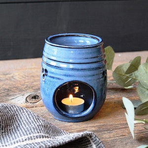 May include: A blue ceramic oil diffuser with a small tea light candle inside. The diffuser has a textured surface and a round opening in the center.