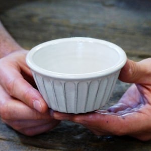 May include: A white ceramic bowl with a fluted design. The bowl is being held by two hands.