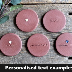 May include: Five terracotta coasters with personalized text examples. The coasters feature the words "Bonnie", "forever loved", and a heart symbol.