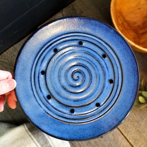 Puede incluir: Un plato de cer&aacute;mica azul con un dise&ntilde;o en espiral y agujeros alrededor del borde. El plato es perfecto para escurrir verduras.