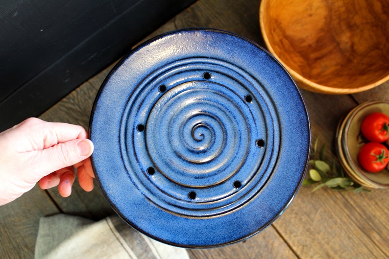 Puede incluir: Un plato de cer&aacute;mica azul con un dise&ntilde;o en espiral y agujeros alrededor del borde. El plato es perfecto para escurrir verduras.