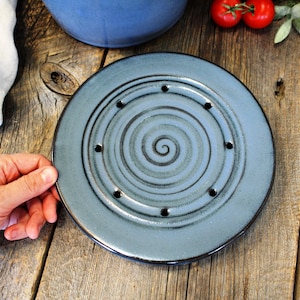 Puede incluir: Un plato de cer&aacute;mica azul con un dise&ntilde;o en espiral y agujeros alrededor del borde. El plato est&aacute; sobre una superficie de madera.