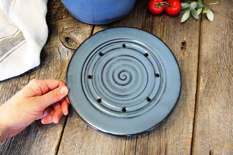 Puede incluir: Un plato de cer&aacute;mica azul con un dise&ntilde;o en espiral y agujeros alrededor del borde. El plato est&aacute; sobre una superficie de madera.