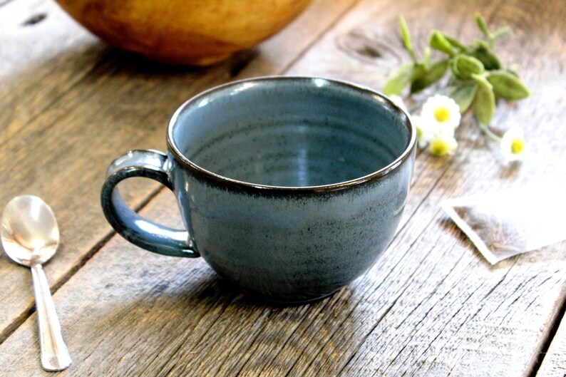 Puede incluir: Una taza de cer&aacute;mica azul con un borde marr&oacute;n oscuro. La taza est&aacute; sobre una superficie de madera.