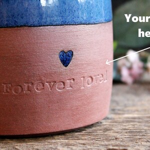 May include: A red and blue ceramic mug with the words "Forever loved" and a blue heart etched into the side.