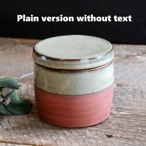May include: A small, round ceramic jar with a lid. The jar is glazed in a light green color with a brown rim. The bottom half of the jar is a reddish-brown color.