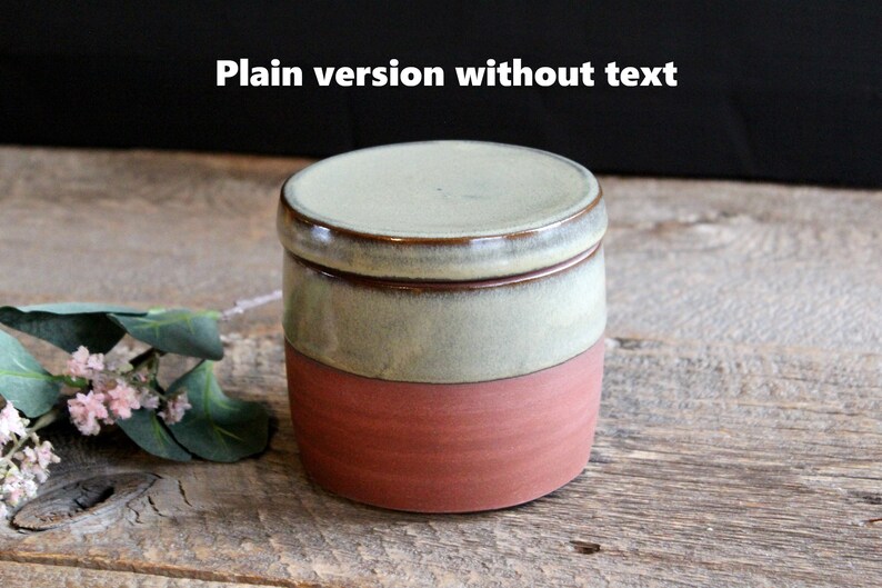 May include: A small, round ceramic jar with a lid. The jar is glazed in a light green color with a brown rim. The bottom half of the jar is a reddish-brown color.