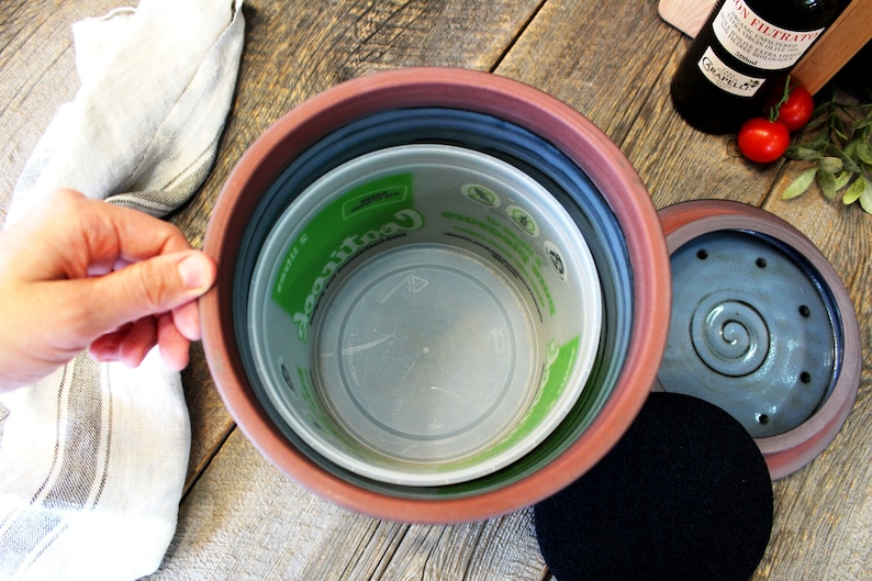 Puede incluir: Un contenedor de compost de terracota con una tapa extra&iacute;ble y un filtro de carb&oacute;n vegetal negro. El contenedor tiene un forro de pl&aacute;stico con una etiqueta verde que dice "Cool Compost".