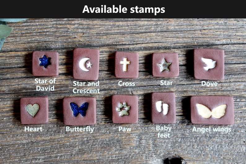 May include: A collection of 10 ceramic tiles with different designs, including a star of David, a star and crescent, a cross, a star, a dove, a heart, a butterfly, a paw print, baby feet, and angel wings. The tiles are all brown with white or gold designs.
