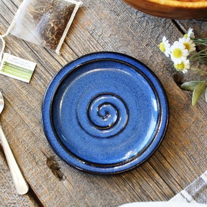 May include: A blue ceramic saucer with a dark blue spiral design. The saucer is on a wooden surface.