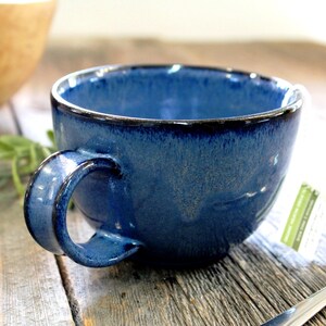 Puede incluir: Una taza de cer&aacute;mica azul con un borde azul oscuro y un esmalte moteado. La taza tiene una forma redondeada y un asa.
