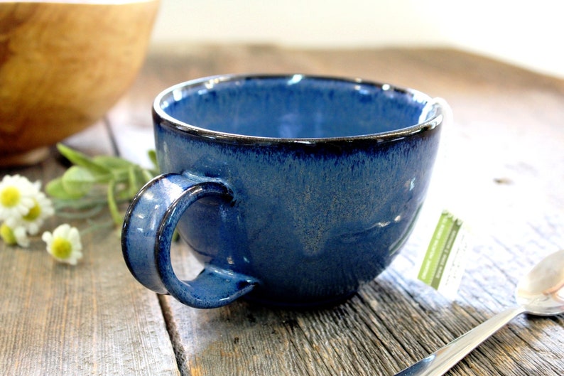 Puede incluir: Una taza de cer&aacute;mica azul con un borde azul oscuro y un esmalte moteado. La taza tiene una forma redondeada y un asa.