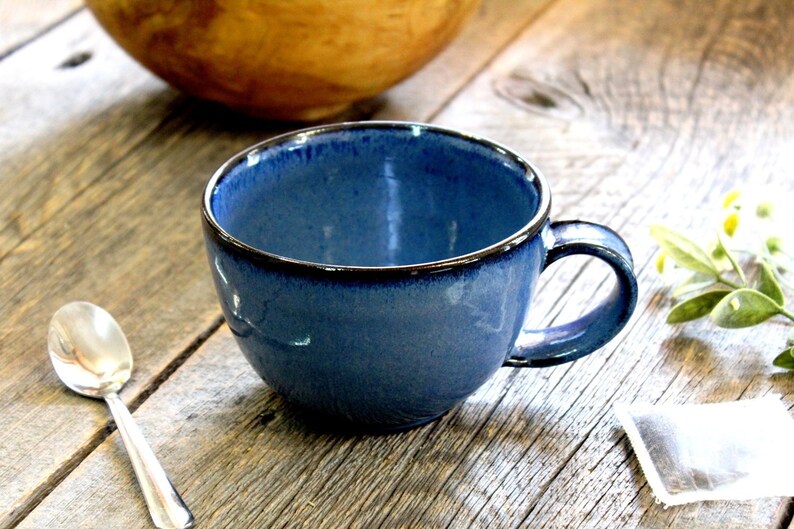 Puede incluir: Una taza de cer&aacute;mica azul con un borde oscuro y un asa. La taza est&aacute; sobre una superficie de madera.