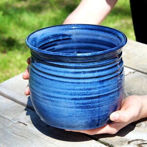 Może przedstawiać: Duży, ciemnoniebieski ceramiczny garnek o zaokrąglonym kształcie i lekko rozszerzającym się brzegu. Garnek ma fakturowaną, lekko nakrapianą glazurę i jest wykonany ręcznie.