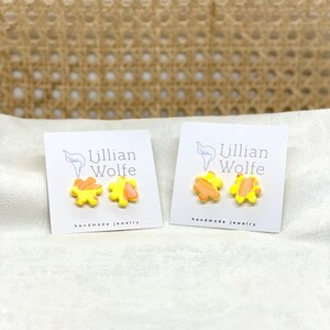 Op de afbeelding: Twee paar gele en oranje bloemvormige oorbellen op witte kaartjes met de tekst "Lillian Wolfe handmade jewelry".