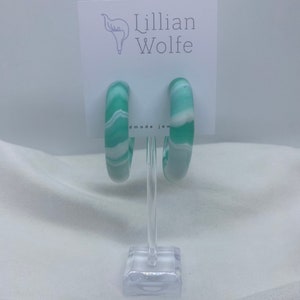 May include: A pair of green and white marbled hoop earrings. The earrings are on a white display stand with a card that says "Lillian Wolfe handmade jewelry".