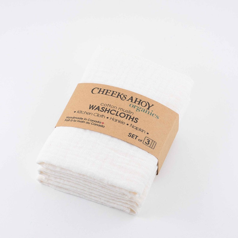 May include: Set of three white cotton muslin washcloths, handmade in Canada. The washcloths are folded and stacked, with a brown label that reads "Cheeks Ahoy Organics, cotton muslin washcloths, Kitchen Cloth, Hankie, Napkin, Set of 3".