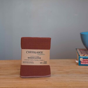 May include: A set of three brown cotton muslin washcloths, folded and stacked. The label reads "Cheeks Ahoy Organics Cotton Muslin Washcloths Kitchen Cloth Hankie Napkin Set of 3 Handmade in Canada Fait &agrave; la main au Canada".