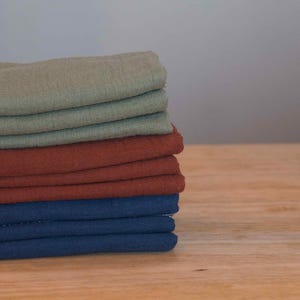 May include: A stack of fabric squares in various colors, including green, brown, and blue. The fabric is folded neatly and appears to be soft and textured.