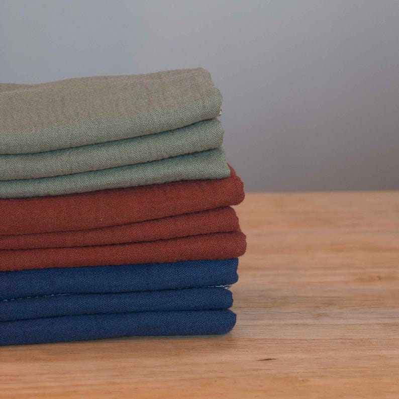 May include: A stack of fabric squares in various colors, including green, brown, and blue. The fabric is folded neatly and appears to be soft and textured.