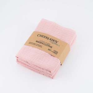 May include: A set of three pink cotton muslin washcloths, folded and packaged with a brown label that reads "CHEEKS AHOY organics cotton muslin WASHCLOTHS SET of 3".