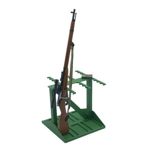 May include: A wooden rifle with a scope and a green strap is displayed on a green stand. The stand has multiple slots for holding the rifle and other accessories. The rifle has a brown wooden stock and a black metal barrel.