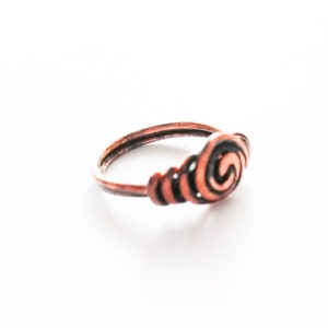 May include: A copper ring with a spiral design. The ring is a simple band with a raised spiral design on the top.