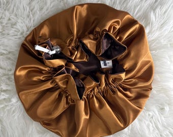 May include: A gold satin bonnet with a brown satin lining. The bonnet is gathered at the top and has a drawstring.