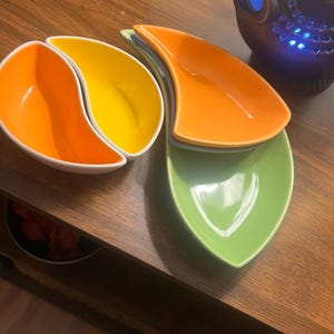 Peut inclure: Ensemble de plats de service en forme de feuille, de couleurs vives. L'ensemble comprend des bols orange, jaune et vert, chacun avec un bord blanc. Idéal pour servir des collations ou de petites portions.