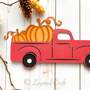 May include: A red wooden truck carrying three orange pumpkins with green vines. The truck has black wheels and a white interior. The image is a fall-themed craft.