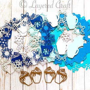 May include: A collection of die-cut paper shapes in winter and holiday themes. Includes snowflakes, mugs, and hot chocolate cups in shades of blue, white, and brown. The Layered Craft logo is visible in the upper right corner.