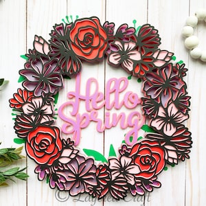 May include: A pink and red paper flower wreath with the words "Hello Spring" in the centre. The wreath is made of layered paper flowers and leaves.