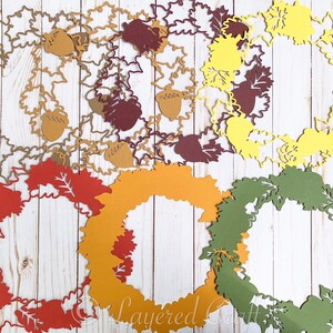 May include: A set of six layered paper wreaths in various autumnal colors, including red, orange, yellow, and green. Each wreath is decorated with a simple leaf design and features a cutout shape.