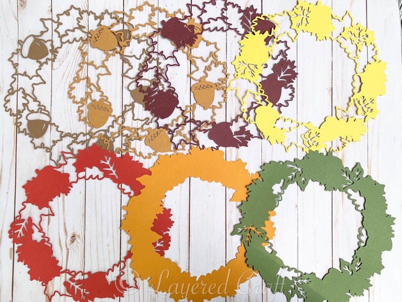 May include: A set of six layered paper wreaths in various autumnal colors, including red, orange, yellow, and green. Each wreath is decorated with a simple leaf design and features a cutout shape.