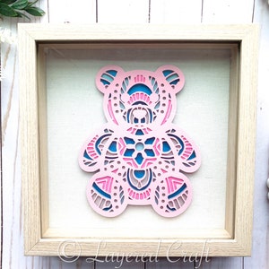 May include: A pink and blue layered paper bear cutout in a wooden frame. The bear is decorated with intricate mandala patterns. The frame has a white background and the text "Layered Craft" is visible in the bottom right corner.