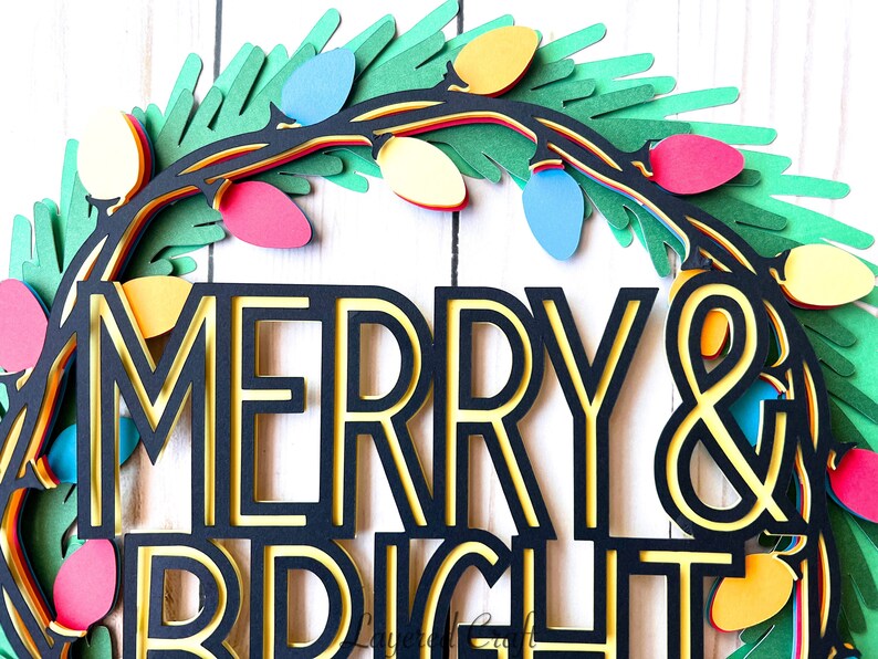 Pu&ograve; includere: Una ghirlanda natalizia di carta a strati con le parole "MERRY & BRIGHT". La ghirlanda presenta un fogliame verde, luci colorate e una combinazione di colori nero e giallo. Il design &egrave; festoso e decorativo.