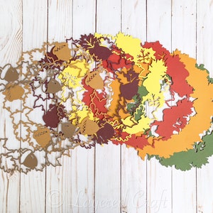 May include: A set of layered paper cutouts in various shades of brown, orange, yellow, and green, featuring leaf and acorn shapes. The cutouts are arranged in a circular pattern, creating a festive autumnal design.
