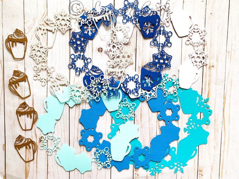 May include: A collection of paper cutouts featuring winter-themed designs. The image includes snowflakes, coffee mugs, and hot chocolate cups in shades of white, blue, and brown. The cutouts are arranged in a circular pattern.