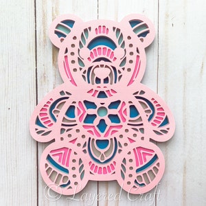 May include: A pink wooden bear with a mandala design in blue, pink, and brown. The bear is cut out in a layered style, creating a 3D effect.