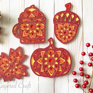 May include: Four layered paper crafts with fall themes. A red and yellow pumpkin, a red and yellow acorn, a red and yellow coffee cup, and a red and yellow maple leaf.