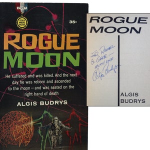 May include: A vintage paperback book cover for the science fiction novel "Rogue Moon" by author Algis Budrys. The cover features a black and red illustration of three figures in a futuristic setting. The book is signed by the author with a personal inscription.