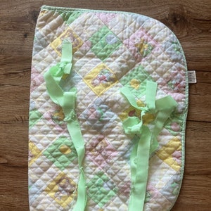 Puede incluir: Una manta de bebé acolchada verde y blanca con un diseño de patchwork que presenta animales de dibujos animados. La manta tiene lazos verdes a cada lado.