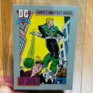 May include: A DC Comics trading card featuring Guy Gardner as Green Lantern. The card shows a dynamic illustration of the superhero in action, with the text "Earth's Mightiest Heroes". The card is encased in a clear protective sleeve.