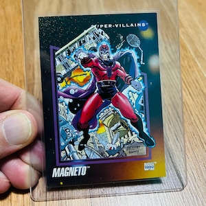 May include: A Marvel trading card featuring Magneto from the "Super-Villains" series. The card shows Magneto in a dynamic pose, wearing a red and purple costume. The card is encased in a clear plastic holder.